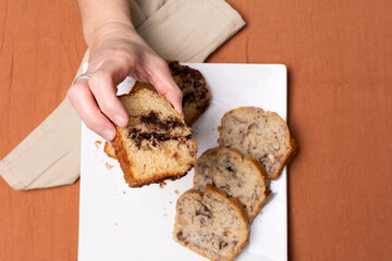 Top view of a hand picking a piece of chocolate bread from a plate.