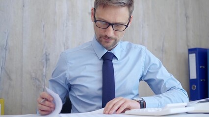 Male accountant with blue t-shirt concentrating while calculating costs and taking notes at his...