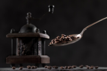 A close-up of fresh coffee beans in a coffee grinder next to coffee beans on a stone tabletop. A spoon pouring coffee
