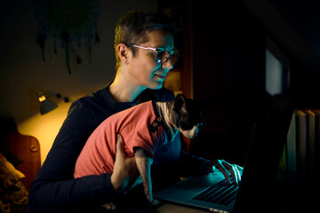 Focused woman working on laptop with Sphynx cat sitting in her arms