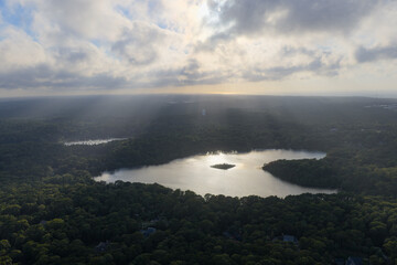 Beams of sunlight fall through low clouds illuminating Pilgrim Lake in Orleans on Cape Cod. This...