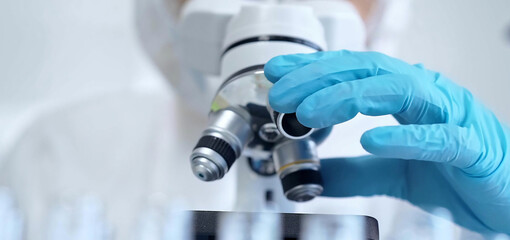Professional scientist in protective gear is using microscope in a laboratory setting, close-up....