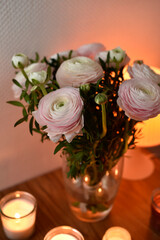 Vertical close-up of pastel ranunculus bouquet lit by soft candlelight. Cozy, stylish floral arrangement perfect for romantic, spa, or home inspiration visuals.