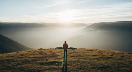 Solitary figure overlooking misty valley at sunrise, casting long shadow on grassy hilltop