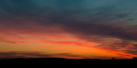 Obraz premium A fiery sunset paints the sky with vibrant colors over a silhouetted landscape.