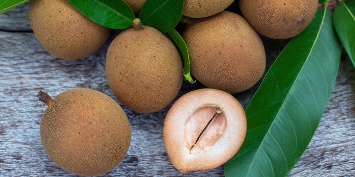 Sapodilla fruits, one cut open, with leaves on a wooden table, capturing a fresh and organic scene.