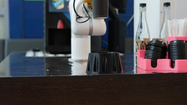 A robotic arm skillfully places a cup of coffee onto a waiting platform. This innovative technology enhances client service during busy hours in the cafe