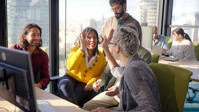 Multicultural team celebrating a milestone with a high five in a bright modern office, showing positive energy, collaboration and motivation while colleagues smile and keep working.
