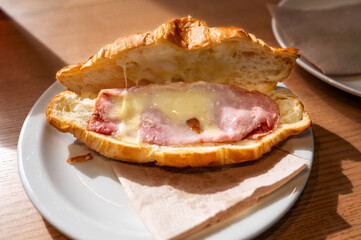 Fresh croissant filled with ham and melted cheese on white plate in cafe. High quality photo