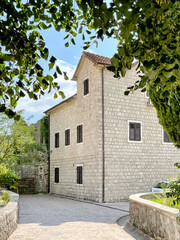 Picturesque waterfront house built from traditional stone, overlooking turquoise waters of the Bay of Kotor. Ideal for travel, vacation, and European coastal living themes.