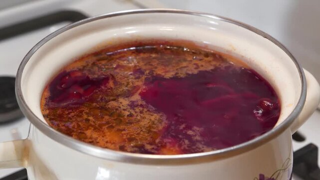 Ukrainian borscht is cooked on gas stove. National dish of Ukraine. Main first course of Ukrainian cuisine. Cooking first courses. Red Ukrainian borscht is boiling in white saucepan
