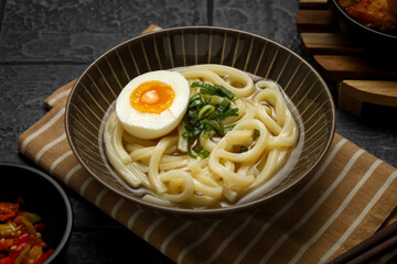 Kake udon with boiled egg. served with sliced chili and tempura.
