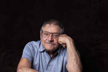 Handsome Caucasian man in his 80s casually sitting and leaning on his fist smiling with confidence