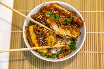 Katsudon Japanese-style cutlet pork (tonkatsu) with egg on rice, fresh chives, and sesame seeds