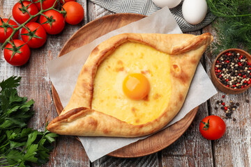 Tasty khachapuri with cheese, egg and other products on wooden table, flat lay