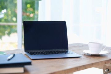Fototapeta premium Home workspace. Laptop, cup of drink and stationery on wooden desk near window indoors