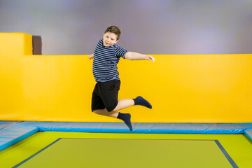 Overweight cute little boy jumping on trampoline indoors in a sport center for kids © Maria
