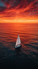 Fototapeta premium A lone sailboat navigates tranquil dark waters under a fiery, vibrant sunset sky, the intense orange and red hues reflecting subtly on the ocean's surface