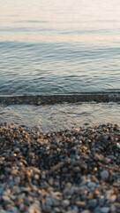 Gentle waves lap a pebble beach at sunset, creating a serene coastal scene