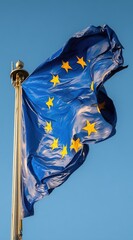 A blue flag with yellow stars flutters against a clear, bright blue sky, attached to a metal pole with a decorative top