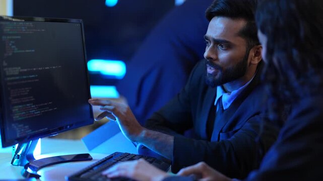 A male and female programmer collaborate on a software project in their tech office. They are working together as a team to write and review code after hours to meet a deadline.