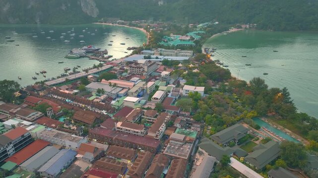 Smooth aerial drone flight westward over the isthmus of Koh Phi Phi Don, Thailand, with a slight downward view showing buildings, coastline, and tropical landscape at sunset