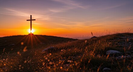 A wooden cross stands on a hilltop at sunset, with a vibrant orange and pink sky in the background.