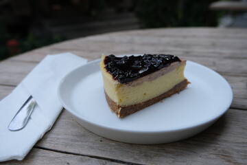 Delicious slice of blueberry-topped cheesecake with layered crust and creamy filling, served on a white plate on a rustic wooden table.
