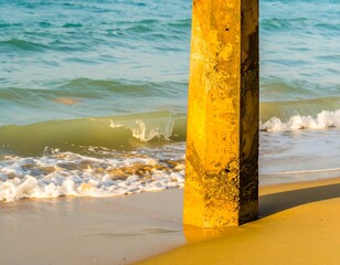 Sunlit beach scene with waves and pier support post
