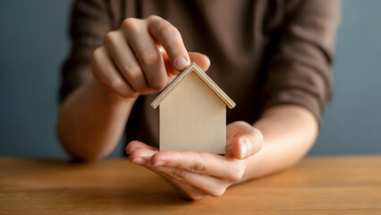 Woman carefully holds miniature wooden house model in cupped hands