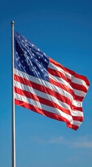 American flag waves in the breeze against a clear blue sky, mounted on a silver pole, displaying stars and stripes