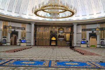 Spacious interior of Jame' Asr Hassanil Bolkiah Mosque featuring a majestic dome, ornate chandelier, prayer carpets, and Islamic architectural elements.
