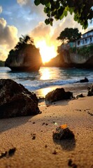 Golden sun shines between two rock formations, creating a scenic coastal landscape. Sandy beach foreground with rocks and warm light filling the sky