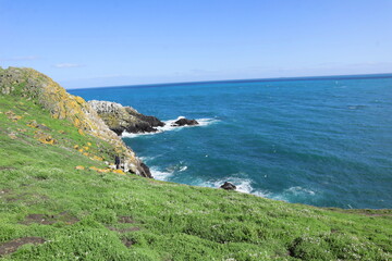Scenic Atlantic coastline at Saltee Island, Ireland, with rocky cliffs, green grass, and turquoise ocean waves, featuring a lone traveler exploring coastal nature