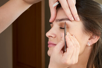 Plucking female eyebrows with tweezers during eyebrow correction in beauty salon