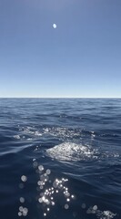 Serene ocean view calm water, distant horizon under clear blue sky with bright sun. Glimmering sunlight sparkles on gentle ripples
