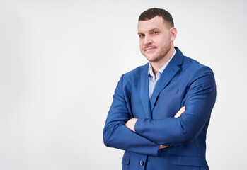 Successful young businessman with crossed arms wearing blue suit with a lovely genuine smile posing against grey background