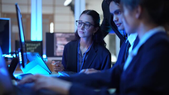 A group of female IT professionals discusses a project in their tech office. They are analyzing data and reviewing code, working as a team to solve a complex problem after hours.