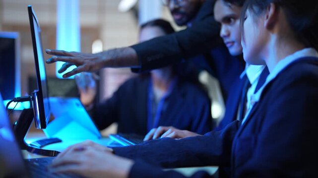 A team of data analysts and software engineers collaborates in a command center, reviewing real time analytics on a tablet while monitoring backend server performance and security logs.