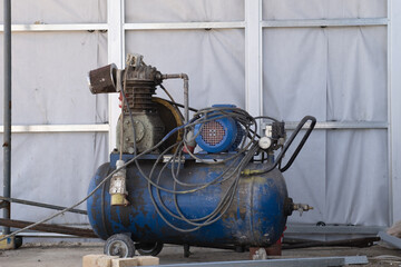 An old blue Working mobile air compressor for painting walls on a construction site. Engineering equipment