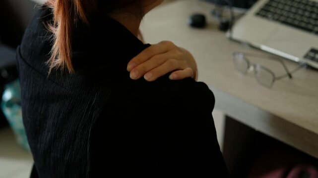 Hands rubbing aching shoulders in office setting 

