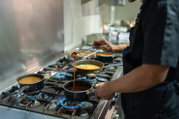 
The image shows a chef working in a professional kitchen, meticulously stirring a sauce in a pot...
