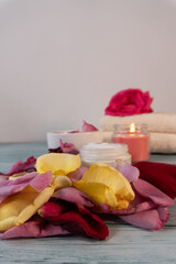 Vertical shot of multi-colored rose petals, skin cream, towels, and a candle on a blue wooden table. Spa