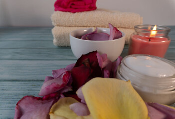Multi-colored rose petals, skin cream, towels, and a candle. Spa
