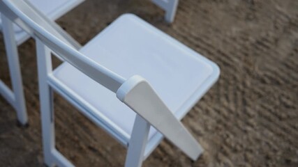 Elegant white chairs are arranged to create a stylish ambiance for a delightful outdoor event on sandy terrain