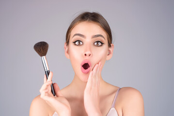 Young woman applies powder on the face using makeup brush. Beautiful girl doing contouring apply...