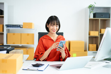 Young Asian woman using tablet in e-commerce office with boxes, laptop, and smile. Perfect for...