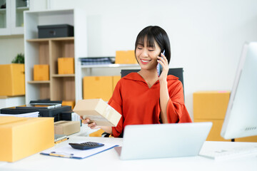 Smiling Asian entrepreneur talks on phone and holds package in modern office.
