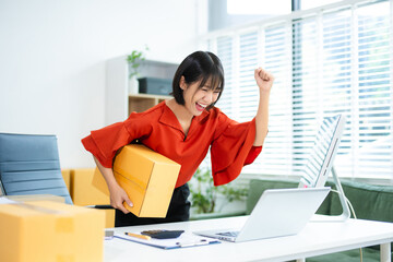 Smiling Asian woman raises fist in joy while holding smartphone. Perfect for business success,...