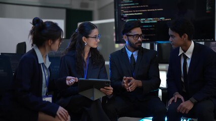 A diverse team of project managers and analysts collaborates on a new strategy. They are reviewing important data on a tablet in a modern corporate command center after hours. - Powered by Adobe